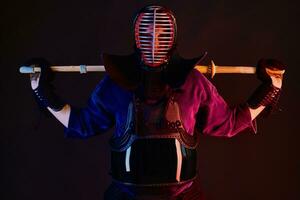 proche en haut tir, kendo combattant portant dans un armure, traditionnel kimono, casque pratiquant martial art avec shinaï bambou épée, noir Contexte. photo