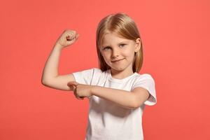 fermer studio coup de une agréable blond peu fille dans une blanc T-shirt posant contre une rose Contexte. photo