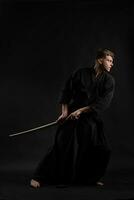 kendo gourou portant dans une traditionnel Japonais kimono est pratiquant martial art avec le shinaï bambou épée contre une noir studio Contexte. photo