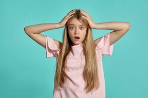 studio portrait de une magnifique fille blond adolescent dans une rose T-shirt posant plus de une bleu Contexte. photo