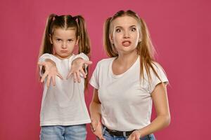 maman et fille avec une marrant queues de cheval, habillé dans blanc t-shirts et bleu denim jeans sont posant contre une rose studio Contexte. fermer tir. photo