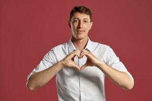 Jeune homme dans une classique blanc chemise est posant plus de une rose Contexte. photo