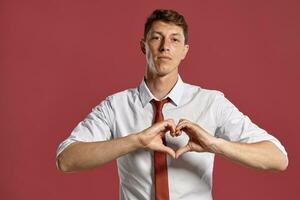 Jeune homme dans une classique blanc chemise et rouge attacher posant plus de une rose Contexte. photo