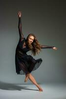 Jeune magnifique Danseur dans noir robe posant sur une foncé gris studio Contexte photo