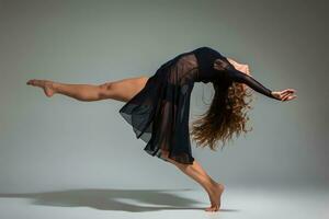 Jeune magnifique Danseur dans noir robe posant sur une foncé gris studio Contexte photo