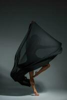 Jeune magnifique Danseur dans noir robe posant sur une foncé gris studio Contexte photo