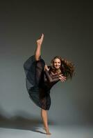 Jeune magnifique Danseur dans noir robe posant sur une foncé gris studio Contexte photo