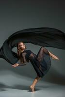 dansant femme dans une noir robe. contemporain moderne Danse sur une gris Contexte. photo