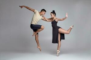 deux athlétique moderne ballet danseurs sont posant contre une gris studio Contexte. photo