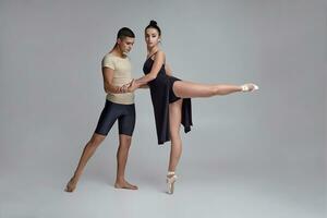 deux athlétique moderne ballet danseurs sont posant contre une gris studio Contexte. photo