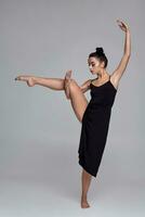 dansant ballerine dans une noir robe. contemporain gracieux performance sur une gris Contexte. photo