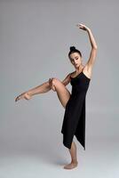 dansant ballerine dans une noir robe. contemporain gracieux performance sur une gris Contexte. photo