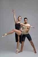 deux athlétique moderne ballet danseurs sont posant contre une gris studio Contexte. photo