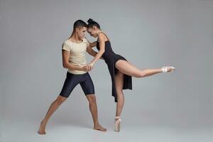 deux athlétique moderne ballet danseurs sont posant contre une gris studio Contexte. photo