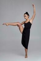 dansant ballerine dans une noir robe. contemporain gracieux performance sur une gris Contexte. photo