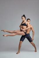 le couple de une Jeune moderne ballet danseurs dans noir costume sont posant plus de une gris studio Contexte. photo