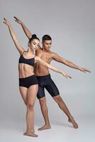 le couple de une Jeune moderne ballet danseurs dans noir costume sont posant plus de une gris studio Contexte. photo