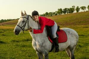 Jeune femme cavalier, portant rouge redingote et blanc culotte, avec sa cheval dans soir le coucher du soleil lumière. photo