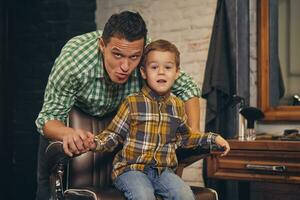 élégant peu enfant séance sur chaise à salon de coiffure avec le sien Jeune père sur Contexte photo