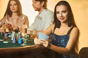 groupe de un élégant gens en jouant poker à le jeux d'argent maison. concentrer sur une luxueux brunette dans une bleu brillant robe photo