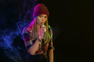 vapoter fille. Jeune branché femme vape e-cig sur noir Contexte. hip hop style. studio coup photo