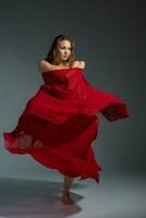 Jeune magnifique Danseur dans rouge robe posant sur une foncé gris studio Contexte photo