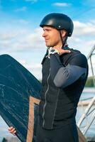 concentré wakeboarder dans plein équipement permanent sur jetée avec conseil, intensément à la recherche une façon photo