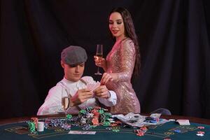 homme en jouant poker à casino séance à table avec piles de puces, argent, Champagne, cartes. célébrer gagner avec femme. noir Contexte. fermer. photo