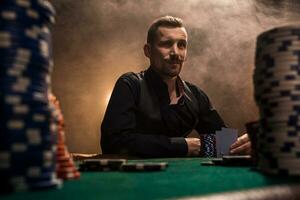 Jeune Beau homme séance derrière poker table avec cartes et frites photo