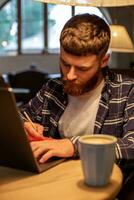 décontractée affaires homme ou pigiste Planification le sien travail sur carnet de notes, travail sur portable ordinateur avec intelligent téléphone, tasse de café sur table à café magasin ou Accueil bureau. photo