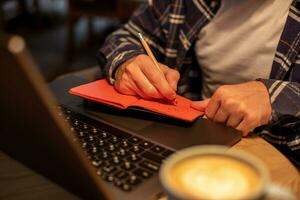 tondu image de décontractée affaires homme ou pigiste Planification le sien travail sur carnet de notes, travail sur portable ordinateur avec intelligent téléphone, tasse de café sur table à café magasin ou Accueil bureau. photo