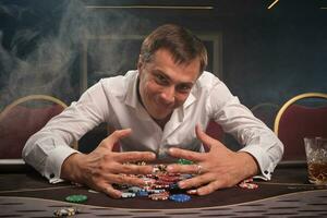 Beau émotif homme est en jouant poker séance à le table dans casino. photo