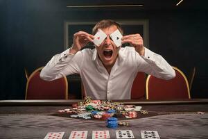 Beau émotif homme est en jouant poker séance à le table dans casino. photo