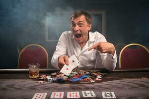 Beau émotif homme est en jouant poker séance à le table dans casino. photo