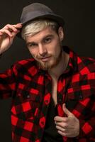 Beau branché Jeune gars à le studio sur noir Contexte. il porte barbe et une plaid chemise photo