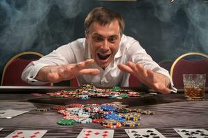 Beau émotif homme est en jouant poker séance à le table dans casino. photo