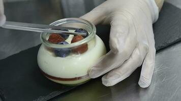 fait maison yaourt avec myrtilles dans une verre pot. main en mettant fraise dans yaourt photo