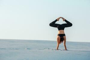 Jeune femme pratiquant inversion équilibrage yoga pose appui renversé sur sable. photo