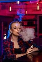 Jeune jolie femme dans une chemise dans une cage fumée un électronique cigarette à le vape bar photo