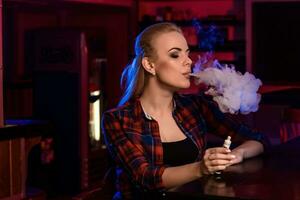 Jeune jolie femme dans une chemise dans une cage fumée un électronique cigarette à le vape bar photo