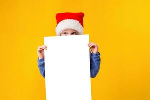 mignonne peu fille dans Père Noël claus chapeau avec une blanc Vide papier feuille. Noël, Noël, Nouveau année, hiver, personnes, publicité, vente concept. photo