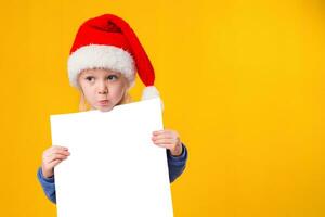 mignonne peu fille dans Père Noël claus chapeau avec une blanc Vide papier feuille. Noël, Noël, Nouveau année, hiver, personnes, publicité, vente concept. photo