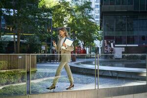 femme d'affaires dans costume, en marchant dans ville, Aller à travail avec portable et documents. entreprise gens concept photo