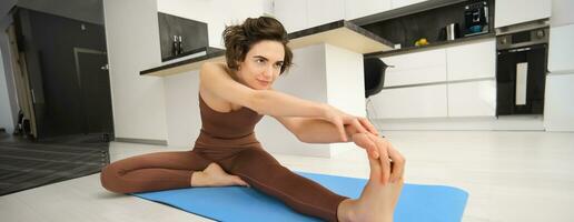 portrait de Jeune en bonne santé femme s'étire sa jambes, penché vers pieds, réchauffer, Faire faire des exercices des exercices à Accueil dans brillant pièce photo