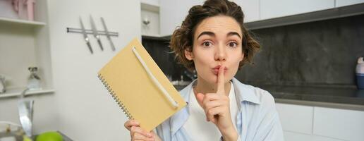 Jeune femme détient sa agenda, spectacles secret, silence geste, presses doigt à lèvres, met sa pensées dans l'écriture photo