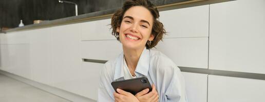 portrait de Jeune adulte femme travaux sur sa tablette, est assis avec carnet sur cuisine sol à maison, études dans confort photo