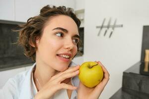 proche en haut portrait de en bonne santé, magnifique Jeune femme en portant un pomme, souriant photo