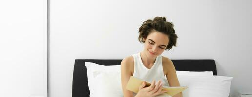 portrait de femme séance dans lit avec journal, l'écriture dans sa agenda, pensées ou sentiments dans le matin, en portant carnet et souriant photo