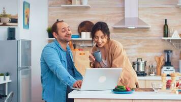 entrepreneur travail sur portable dans cuisine et épouse en portant une tasse de café à la recherche à le sien travail. mari et épouse cuisine recette aliments. content en bonne santé ensemble mode de vie. famille recherche pour en ligne repas. santé Frais salade photo