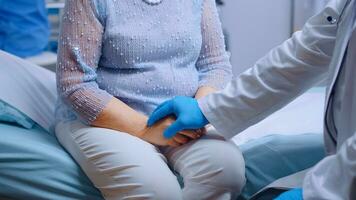 proche en haut de médecin mains dans bleu protecteur gants réconforter une stressé vieux femme séance sur hôpital lit dans moderne privé clinique. global pandémie coronavirus covid-19 soins de santé pandémie photo